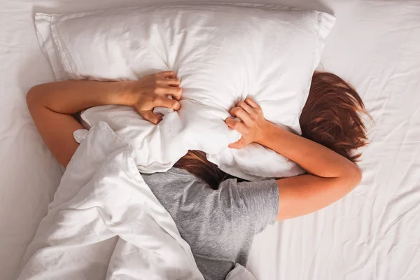 Жінка лежить у ліжку і покриває голову подушкою . — стокове фото