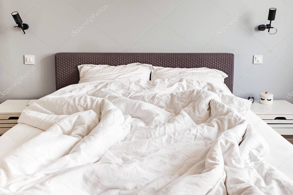 Unmade messy bed with white bedsheet in the morning.