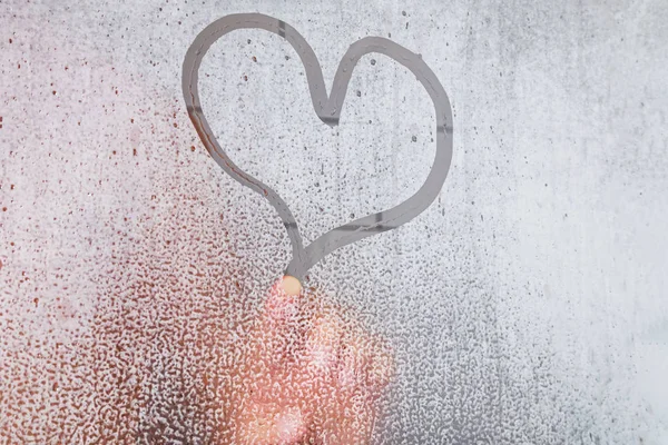 Adult person finger drawing a heart shape on the misted glass with drops in the bathroom. — Stock Photo, Image