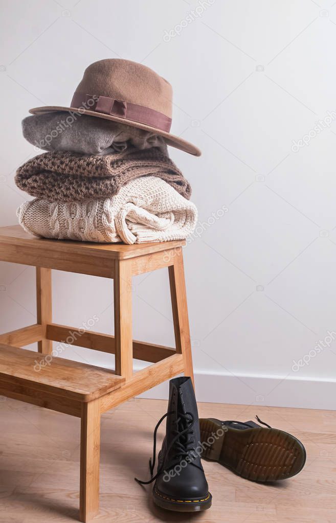 Pile of folded warm sweaters, felt hat and boots.