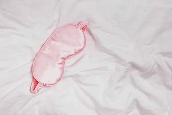 Silk Pink Eye Mask liggande på vita sängkläder på morgonen, — Stockfoto