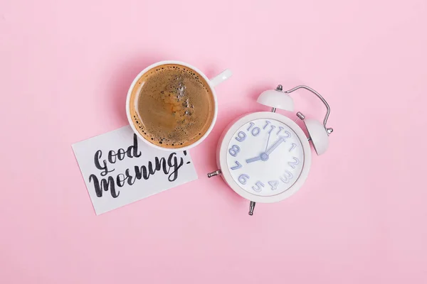 Analog çalar saat, kahve fincanı ve pembe arka plan üzerinde metin günaydın nota. — Stok fotoğraf