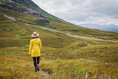 Yağmurlu dağlarda şapka ve yağmurluk yürüyüş genç kadın gezgin