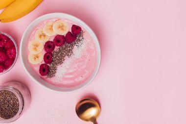 Çilek ile Smoothie kase, chia tohumu, muz ve pembe arka plan üzerinde ahududu ile tepesinde