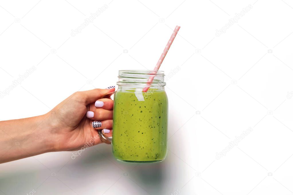 Womans hand holding a glass jar with green smoothie