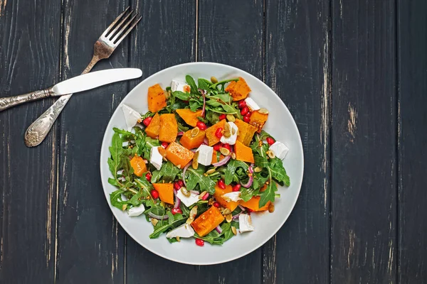 Salad with pumpkin, arugula, feta cheese and pomegranate seeds on black wooden table — Stock Photo, Image