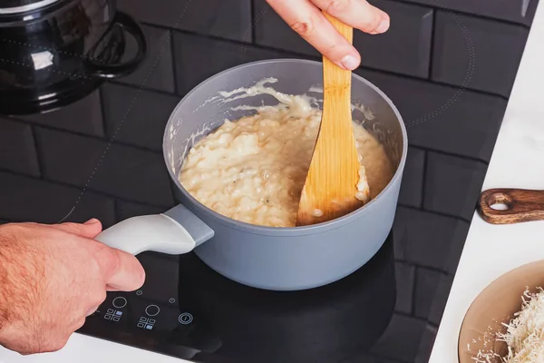 Mão mistura risoto cremoso com queijo em um pote close-up . — Fotografia de Stock
