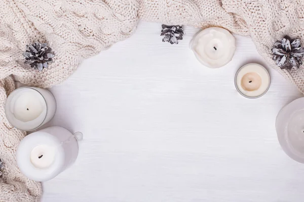 Gebreide trui of sjaal, kaarsen en dennenappels op witte bakgrond. — Stockfoto