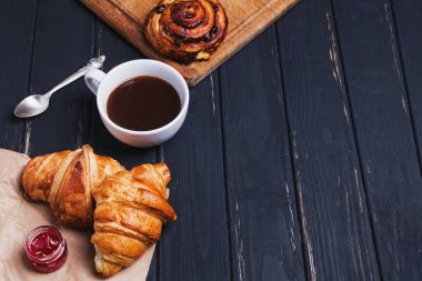 Kahve ve taze kruvasanlar siyah masada.