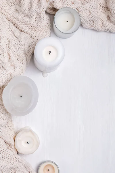 Creative composition with white candles and knitted sweater on the white wooden table