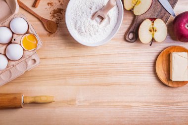 Ahşap masadaki elmalı turta için malzemeler ve araçlar, üst görünüm.