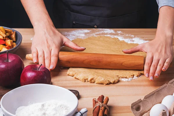 Жінки розкачують тісто для яблучного пирога на дерев'яному столі крупним планом — стокове фото