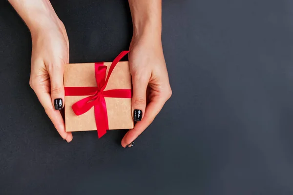 Vrouwen handen houden een geschenkdoos met rode strik op zwarte achtergrond — Stockfoto