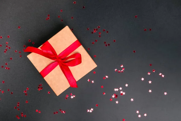 Giftbox with red bow over black background with red star shaped confetti — Stock Photo, Image