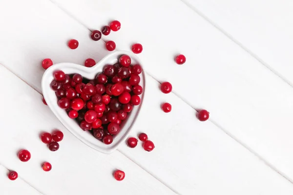 Fresh cranberries in a heart shaped bowl on white wooden table — Stock Photo, Image