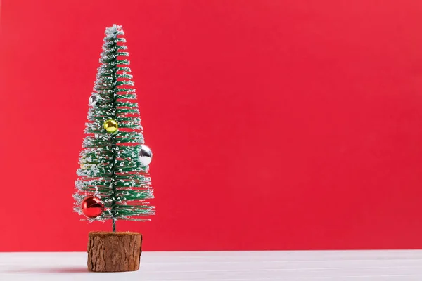 Pequena árvore de Natal artificial decorada com bolas e neve no fundo vermelho — Fotografia de Stock