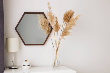 Ahşap aynanın yanında duran şeffaf cam vazoda kuru kamışlı..