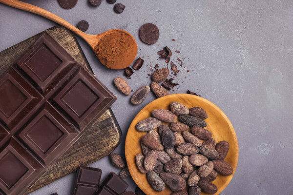 Chocolate bar and drops, cocoa beans and powder on grey background