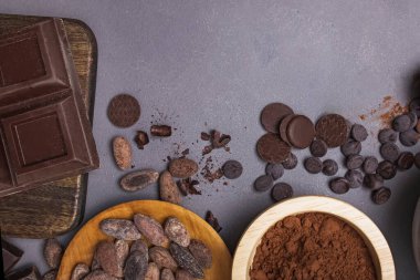 Çikolata parçaları ve damlalar, kakao çekirdekleri ve gri arka planda toz.