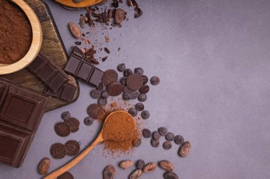Çikolata parçaları ve damlalar, kakao çekirdekleri ve gri arka planda toz.