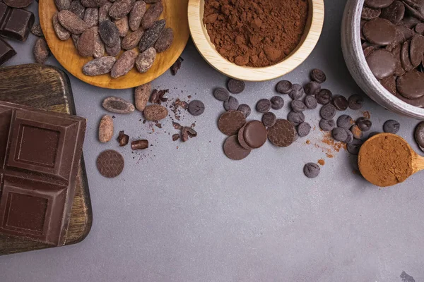 Trozos y gotas de chocolate, granos de cacao y polvo sobre fondo gris — Foto de Stock