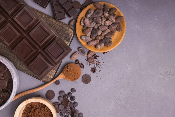 Pezzi e gocce di cioccolato, fave di cacao e polvere su fondo grigio — Foto Stock
