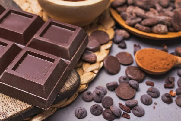 Trozos y gotas de chocolate, granos de cacao y polvo sobre fondo gris — Foto de Stock