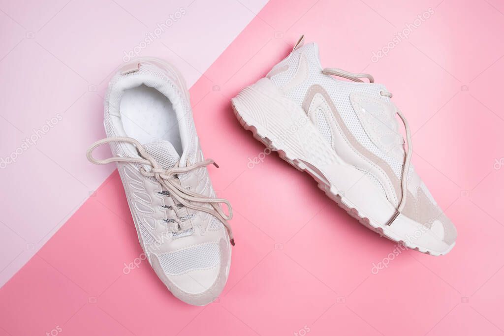 Stylish beige womens sneakers on pink background.