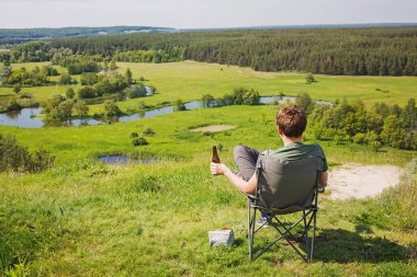 Güzel manzaralı kamp koltuğunda dinlenen bir adam.