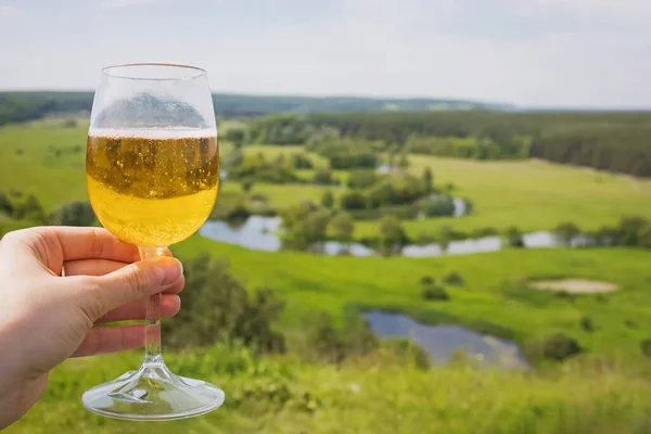 Ręczne trzymanie glazury bocznej lub innego alkoholowego napoju musującego z widokiem na piękną zieloną łąkę na wsi — Zdjęcie stockowe