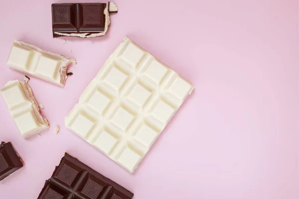 Białe i czarne tabliczki czekolady i kawałki na różowym tle, widok z góry — Zdjęcie stockowe