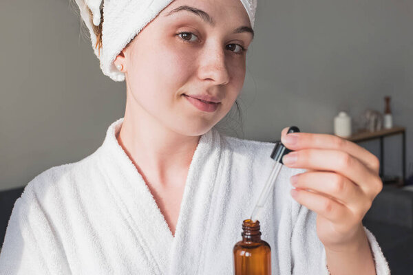 Молодая женщина после душа собирается применить сыворотку красоты
