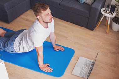 Genç adam oturma odasında yoga yapıyor.