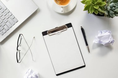 Boş kağıtlı pano kahve, bardak, dizüstü bilgisayar ve buruşuk kağıt dolu masa.