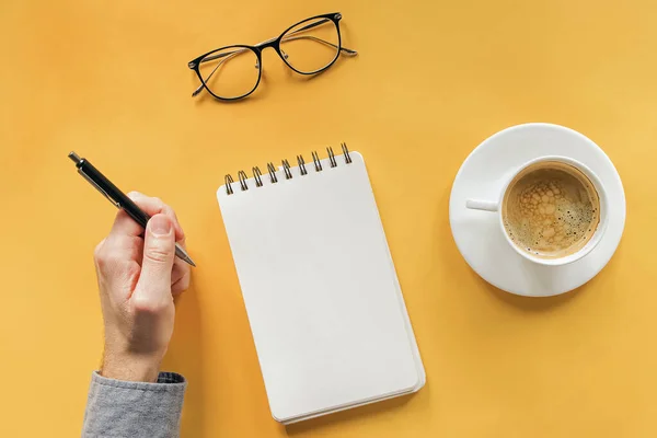 Mans hand hoding pen near blank notepad on the table with coffee and glasses — Stock Photo, Image