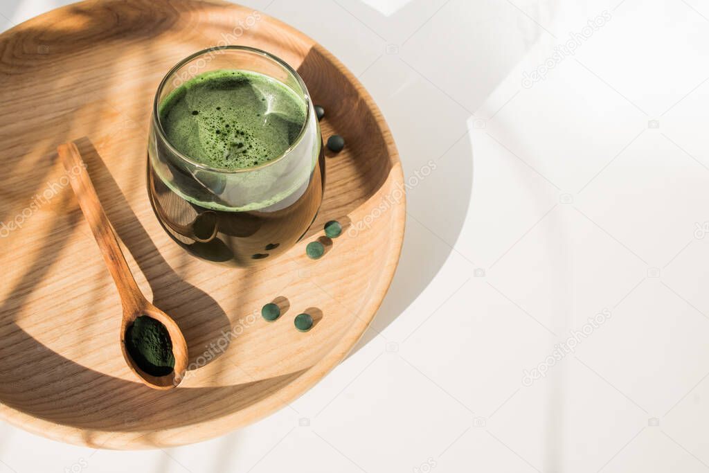 Spirulina or chlorella in a glass. Green food supplement, healhy lifestyle. Natural light and plant shadow on the table