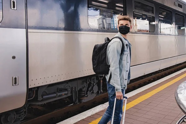 Young man wearing protective face mask standing on the railway station near the train