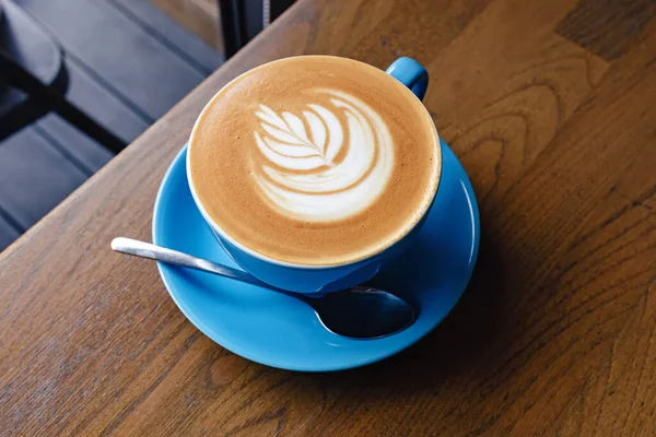 Bir fincan taze kapuçino ve ahşap masa üzerinde latte sanatı.