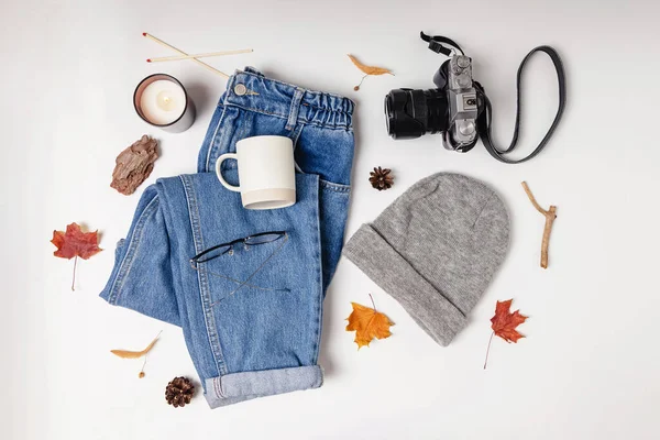 Autumn flat lay. Feminine clothing, camera and yellow leaves on white table, top view