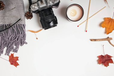 Beyaz masada yaratıcı sonbahar kompozisyonu. Atkı, kamera, mum ve sarı yapraklar, üst manzara