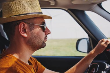 Hasır şapkalı genç yakışıklı adam araba kullanıyor.