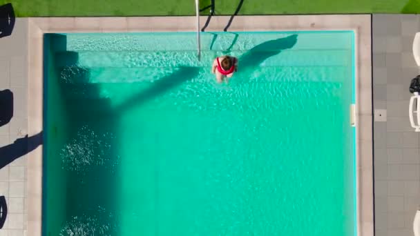 Pohled shora jako žena v červených plavkách plave v bazénu