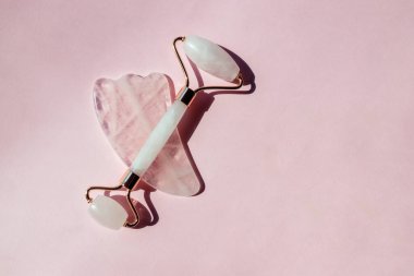 Yeşim silindir ve gua sha aracı. Pembe arka planda yüz masajı araçları
