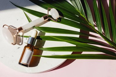Yüz masajı ve bir şişe nemlendirici serum için Jade Roller. Sağlık, cilt bakımı. Dümdüz uzanmış güneş ışığında