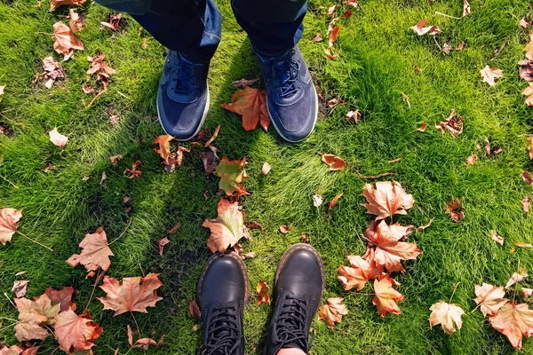 Man en vrouw benen in sneakers en laarzen staan op de grond met gele herfstbladeren — Stockfoto