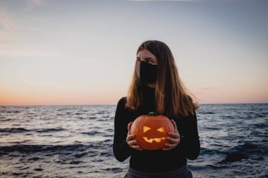 Koruyucu maske takan kadın elinde balkabağı tutuyor.