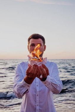 Denizin arka planında yanan beyaz kağıt tutan bir adam.