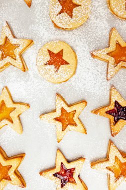 Yıldız şeklinde renkli reçelle dolu, toz şekerle serpiştirilmiş kurabiyelerin üst görüntüsü. Kurabiyeler bir yemek tepsisine konur. Ev yapımı, şenlikli görüntülerini vurgularlar..