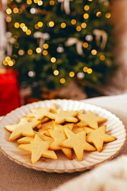 Bir tabak yıldız şekilli kurabiye, güzel ışıklandırılmış bir Noel ağacının önünde sergilenerek sıcak ve şenlikli bir tatil atmosferi yaratıyor..