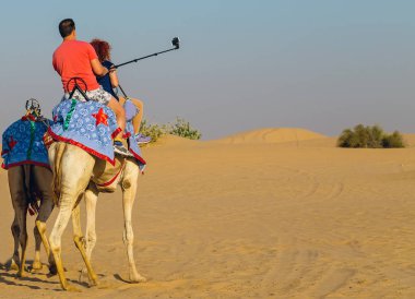Turist konumlar kum çöl safari deve bir selfie kullanarak sopa shot cep telefonu, turist alınır geleneksel Bedevi eyer deveye biniyor.